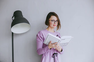 a woman standing next to a lamp reading a book