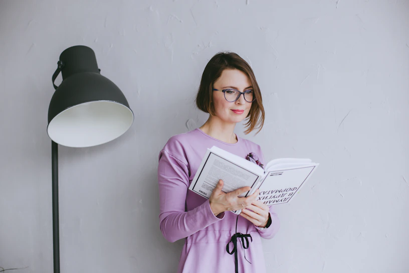 a woman standing next to a lamp reading a book