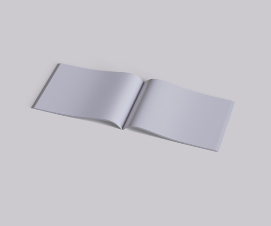 An open blank book lies flat against a solid, neutral background. The pages are empty, displaying a smooth, even texture, and the book's spine is slightly visible.