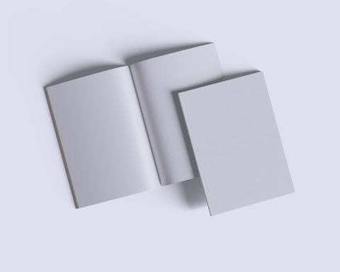 Three plain books are arranged on a light gray background. Two are closed, and one is open in the center, displaying blank pages.