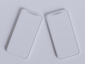 Two modern smartphones with sleek, minimalistic design are placed side by side against a light gray background. Their screens are off, reflecting the ambient light, and they feature a simple, elegant look with rounded edges and a clean interface.