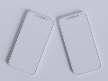 Two modern smartphones with sleek, minimalistic design are placed side by side against a light gray background. Their screens are off, reflecting the ambient light, and they feature a simple, elegant look with rounded edges and a clean interface.