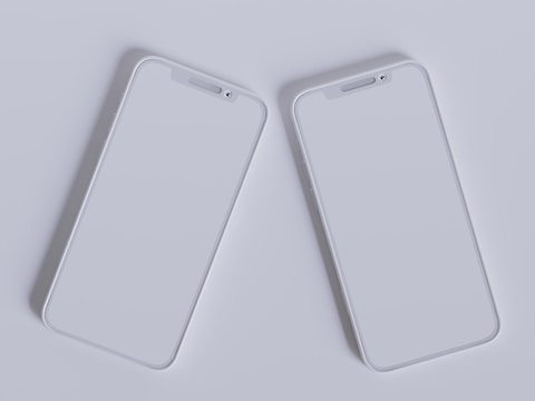 Two modern smartphones with sleek, minimalistic design are placed side by side against a light gray background. Their screens are off, reflecting the ambient light, and they feature a simple, elegant look with rounded edges and a clean interface.