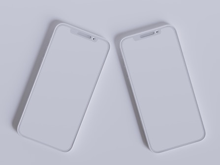 Two modern smartphones with sleek, minimalistic design are placed side by side against a light gray background. Their screens are off, reflecting the ambient light, and they feature a simple, elegant look with rounded edges and a clean interface.