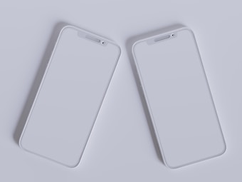 Two modern smartphones with sleek, minimalistic design are placed side by side against a light gray background. Their screens are off, reflecting the ambient light, and they feature a simple, elegant look with rounded edges and a clean interface.