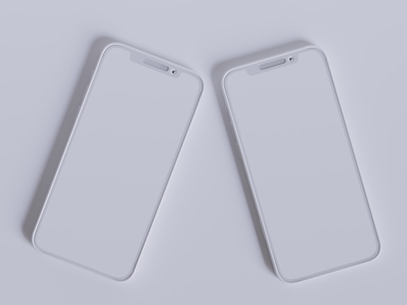 Two modern smartphones with sleek, minimalistic design are placed side by side against a light gray background. Their screens are off, reflecting the ambient light, and they feature a simple, elegant look with rounded edges and a clean interface.