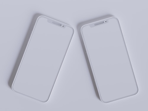 Two modern smartphones with sleek, minimalistic design are placed side by side against a light gray background. Their screens are off, reflecting the ambient light, and they feature a simple, elegant look with rounded edges and a clean interface.