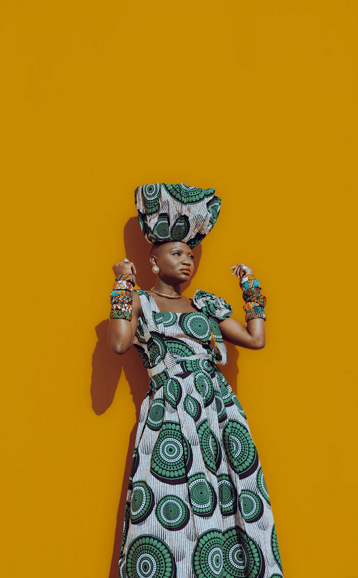 Woman in a structured dress and headwrap against a yellow wall