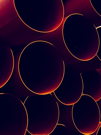 A collection of large, cylindrical pipes stacked together in a pattern. The edges of the pipes are highlighted with a warm orange glow, contrasting with the dark interiors.