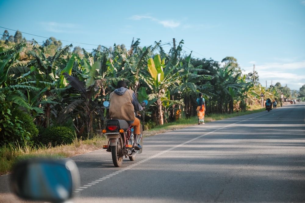 a man riding a bike down a street next to a lush green forest