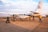 A small aircraft with the registration 5X-BXW and AeroLink branding is stationed on a tarmac. Several people are seen around the plane, some carrying luggage and others walking towards it. The surrounding area appears to be an airport with a wide view of the sky and distant landscape.