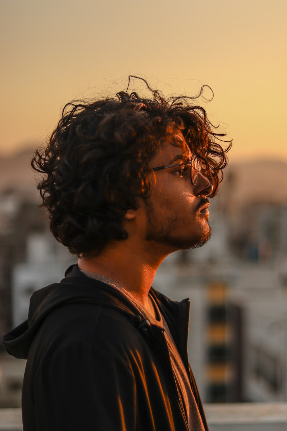 a man with curly hair and glasses looking off into the distance