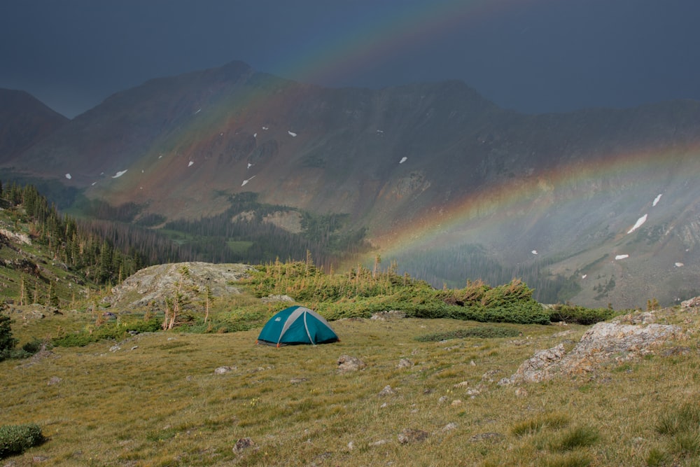 a tent in a field with a rainbow in the background