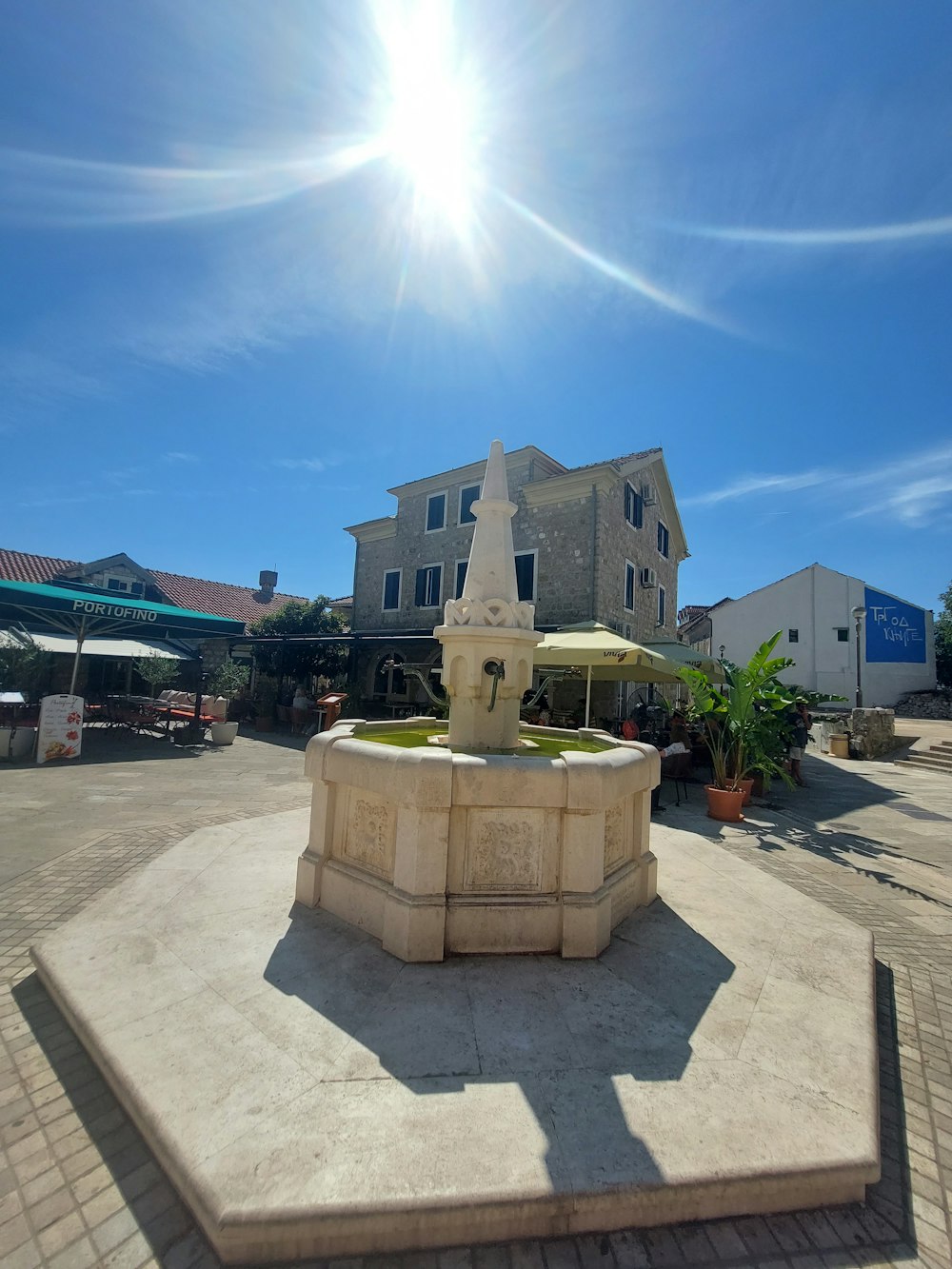 the sun shines brightly over a fountain in the middle of a courtyard