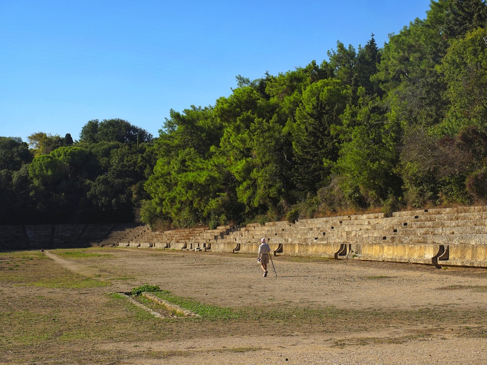 two people walking on a dirt road near a stone wall