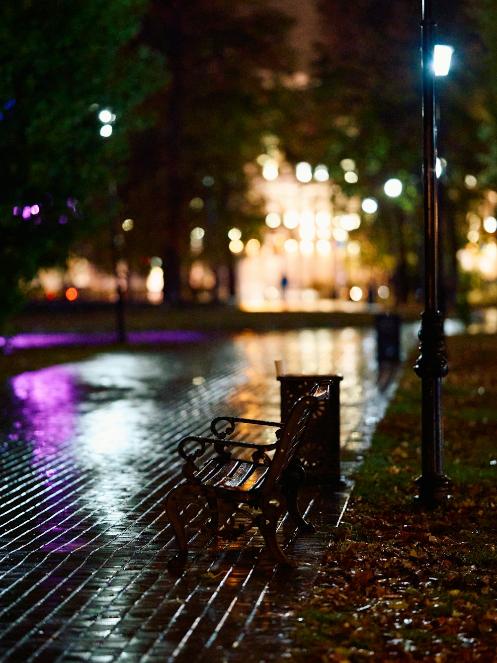 a park bench sitting on a wet sidewalk at night