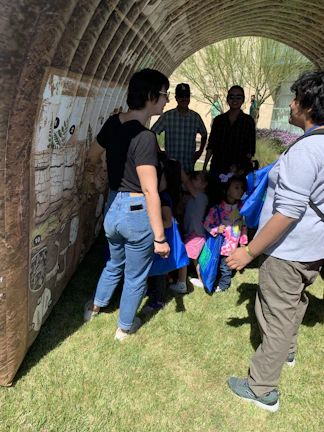 A group of school-age youth engaged in a collaborative outdoor learning activity under bright sunlight.
