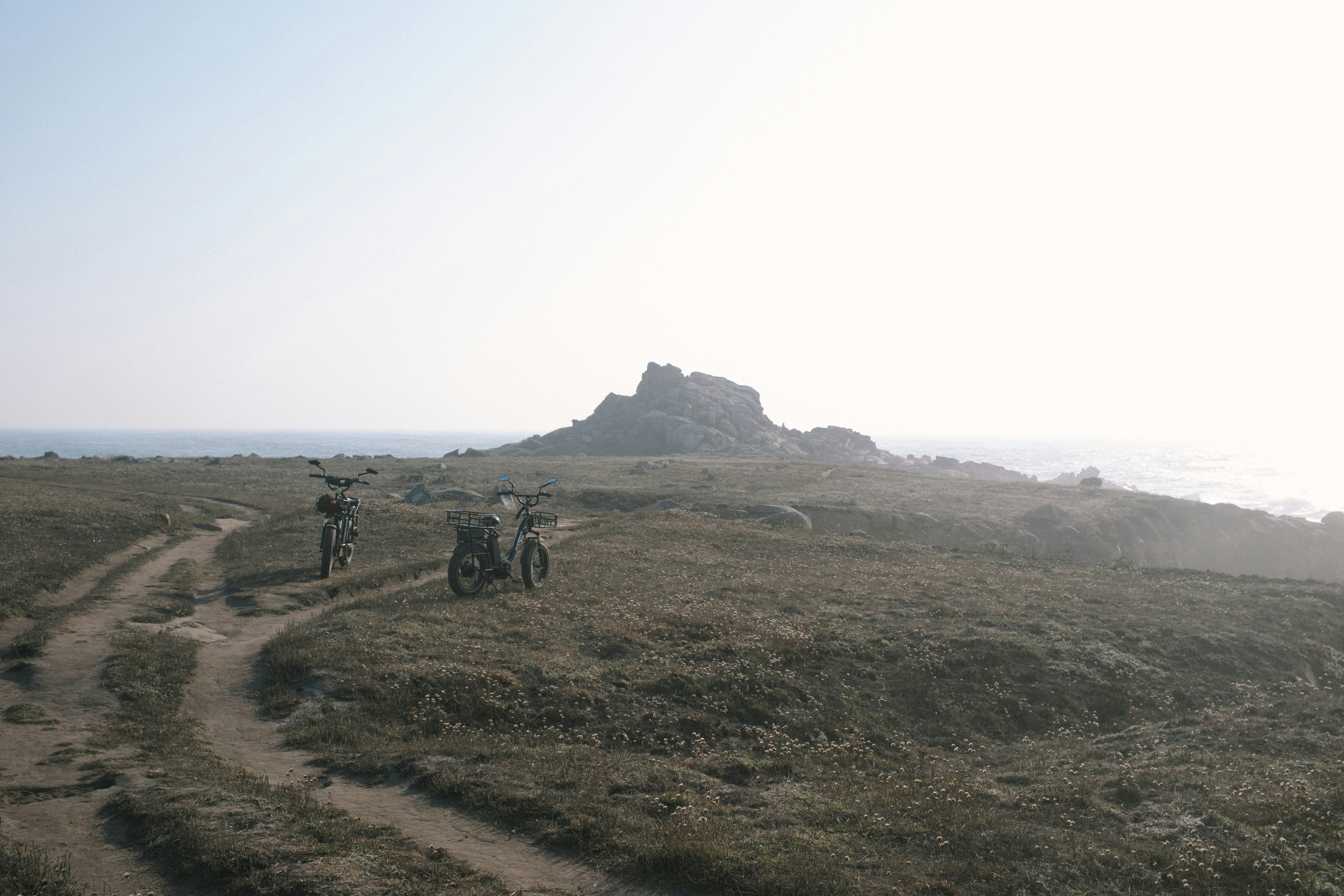 two motorcycles parked on a dirt road near the ocean