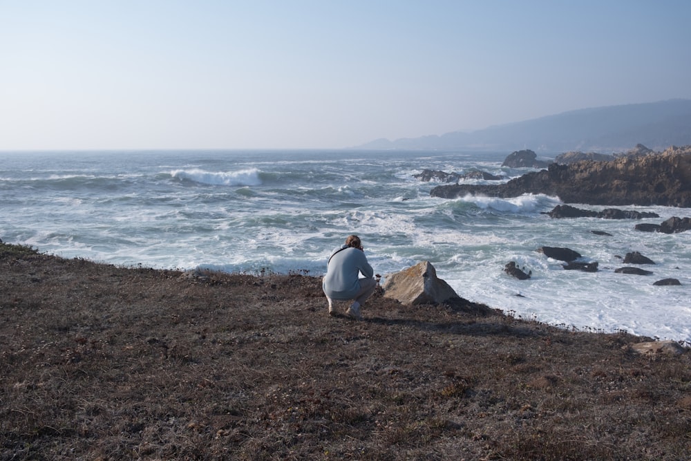 uma pessoa sentada em uma rocha perto do oceano