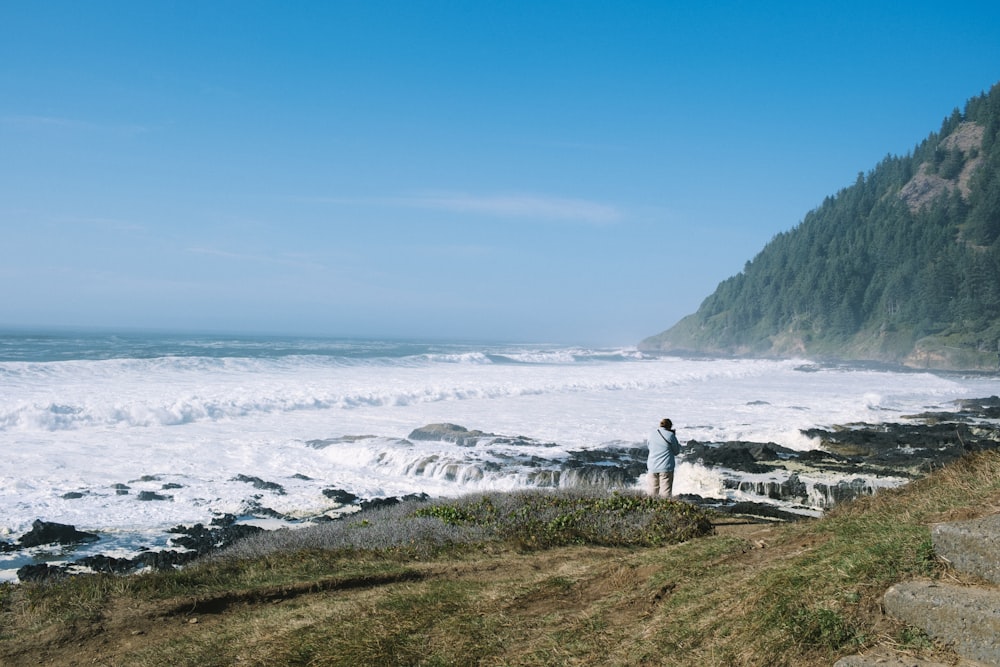 a man standing on top of a cliff next to the ocean