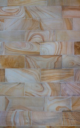A pattern of rectangular tiles with swirling natural stone textures in varying shades of beige, brown, and cream.