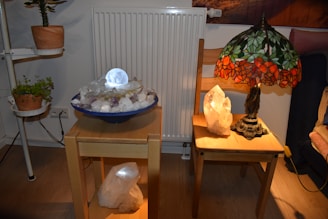 Ann smiling warmly while holding a glowing crystal candle in a cozy, sunlit room filled with plants.