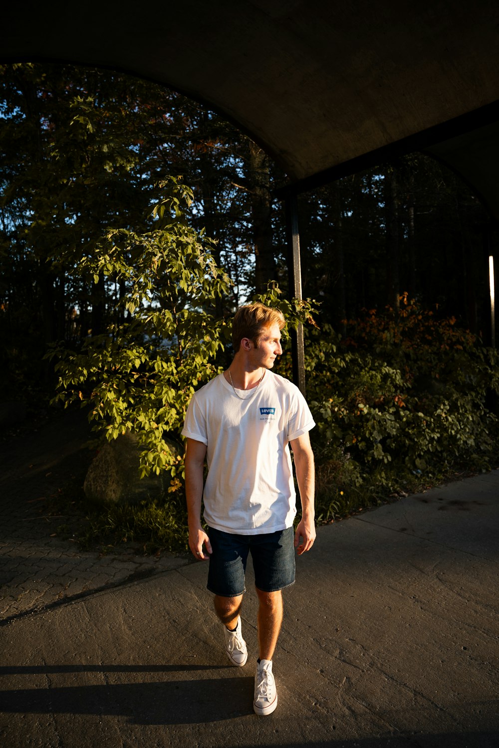 a man in a white shirt is walking under a bridge