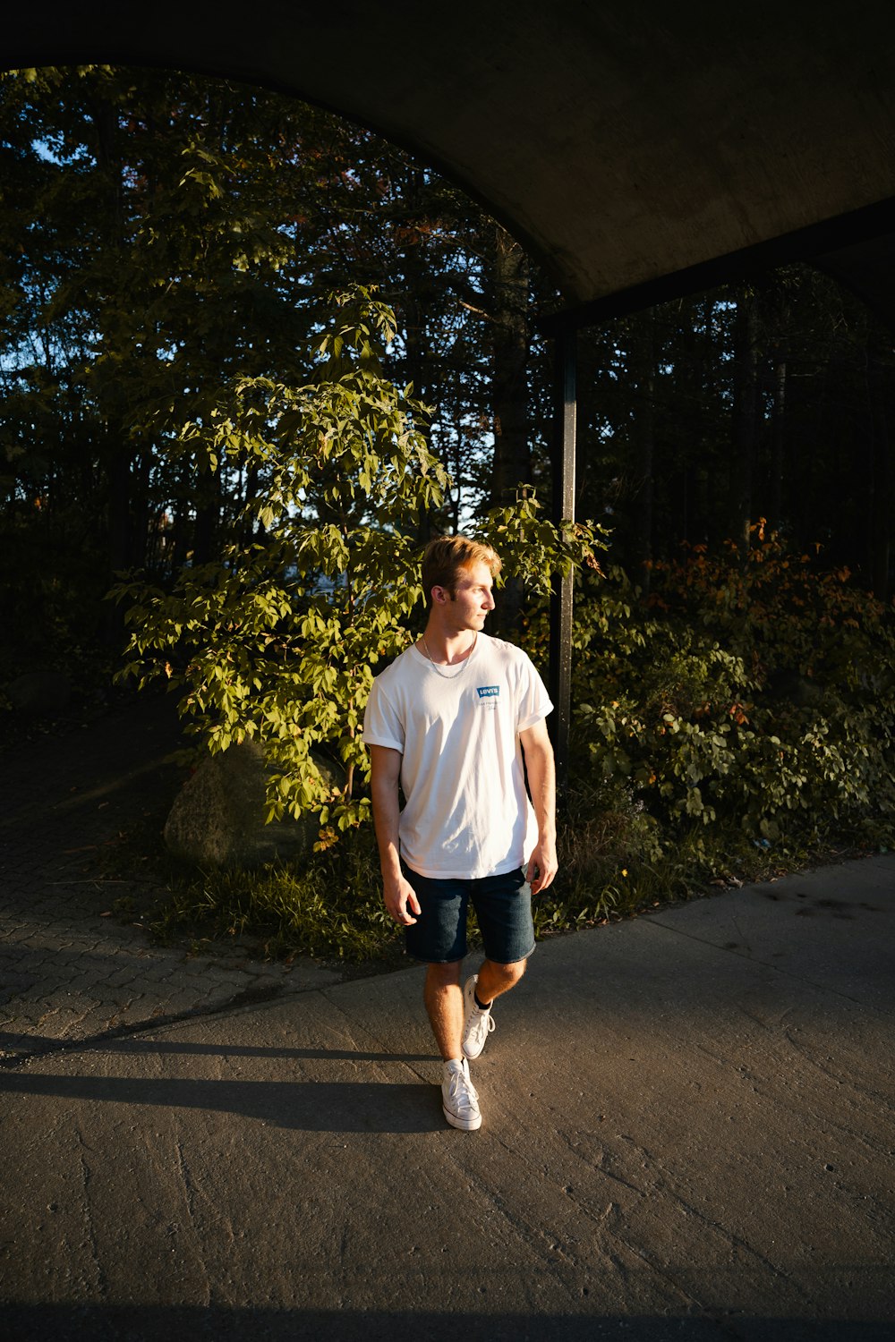 a man walking down a sidewalk under a bridge