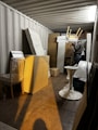 A storage container filled with various items including wrapped furniture and stacked boxes. A person is seen organizing the contents, holding a chair above other items.