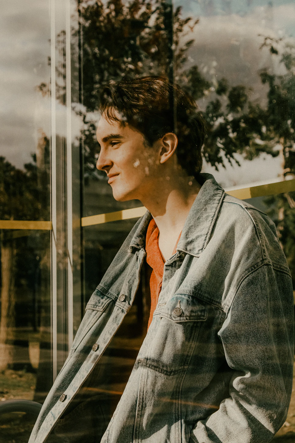 Young man stands by window with white blinds, gazing off to the side slowly