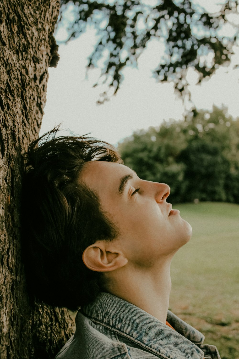 a young man leaning against a tree in a park