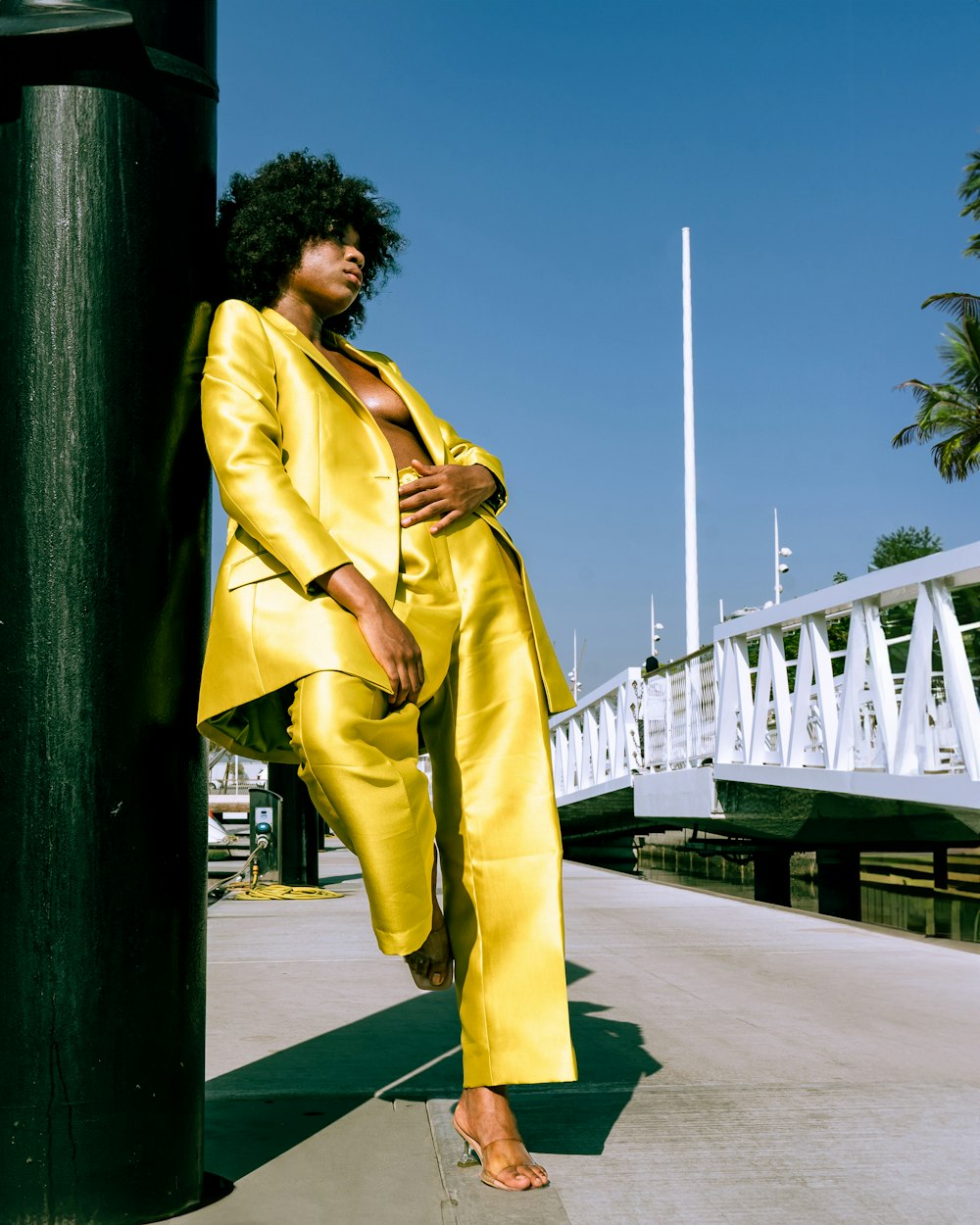 a woman in a yellow suit leaning against a pole