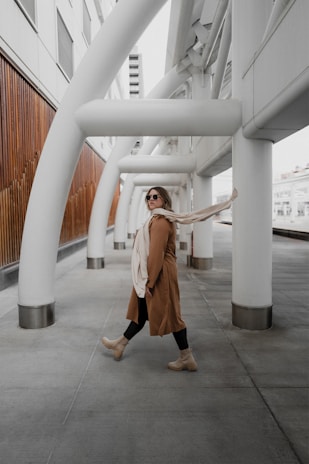 A model walking confidently in a modern, structured coat with clean lines, set against a sleek architectural background.