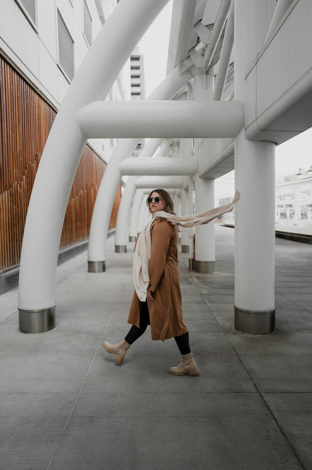 a woman walking down a sidewalk next to tall white pillars