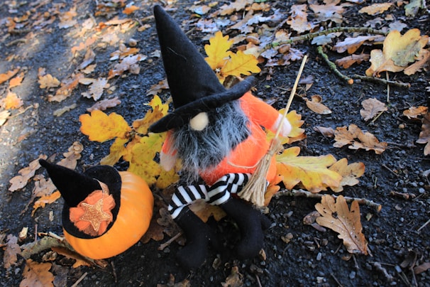 A close-up of a friendly witch animatronic waving from the corner of the garage, surrounded by fall leaves.