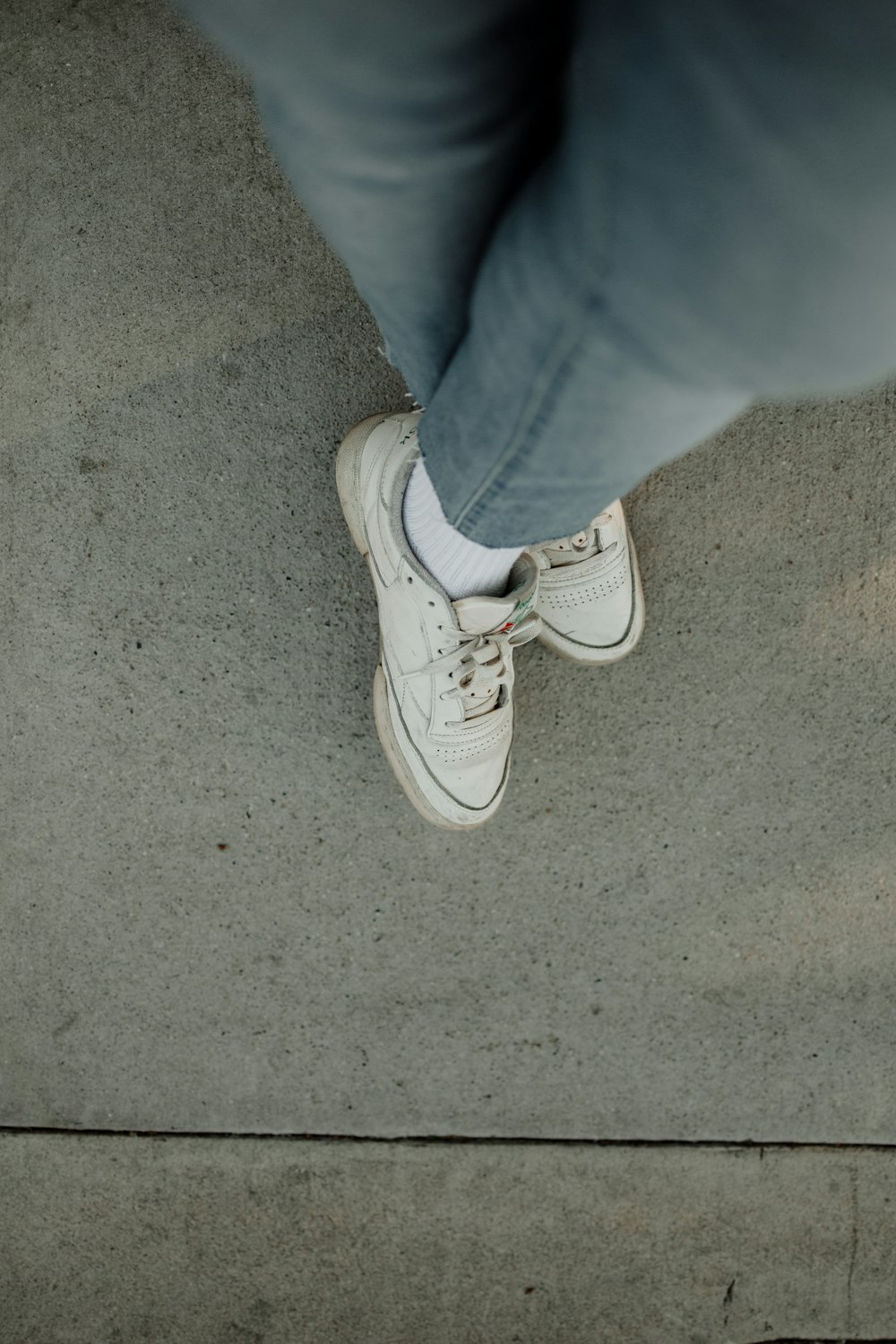 uma pessoa em pé em uma calçada usando sapatos brancos