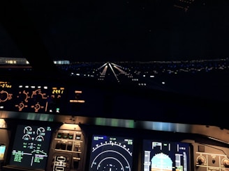 An aircraft cockpit during a night landing is visible, with illuminated control panels and flight instruments. The runway ahead is lit by runway lights, creating a visually striking perspective.