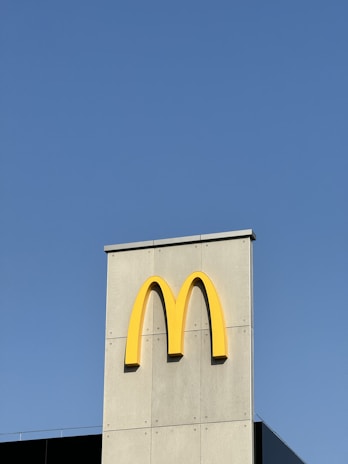A gray building facade prominently features a large yellow letter M, symbolizing a global fast-food brand. The clear blue sky dominates the background, providing a stark contrast to the building.