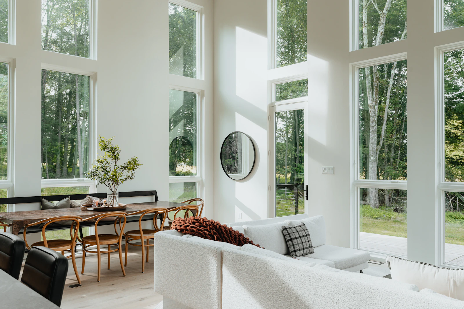 A bright living room ringed with tall windows looking out into green trees
