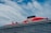 A large cruise ship with a prominent red section on the upper deck and black exhaust funnels. The ship has multiple decks and features the brand name 'Virgin' prominently on the red section. The sky is partly cloudy with patches of blue visible.