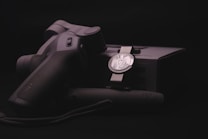 A sleek, ergonomically designed stabilizer or gimbal rests against its packaging, highlighted by soft lighting that emphasizes the matte black and metallic textures. The branding logo is subtly visible on both the device and the box, suggesting a focus on quality and technology.