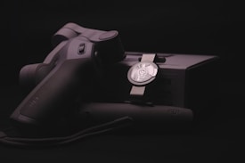 A sleek, ergonomically designed stabilizer or gimbal rests against its packaging, highlighted by soft lighting that emphasizes the matte black and metallic textures. The branding logo is subtly visible on both the device and the box, suggesting a focus on quality and technology.