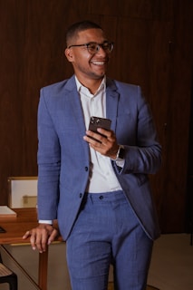 A stylish man wearing a tailored shirt, smiling while holding a smartphone.