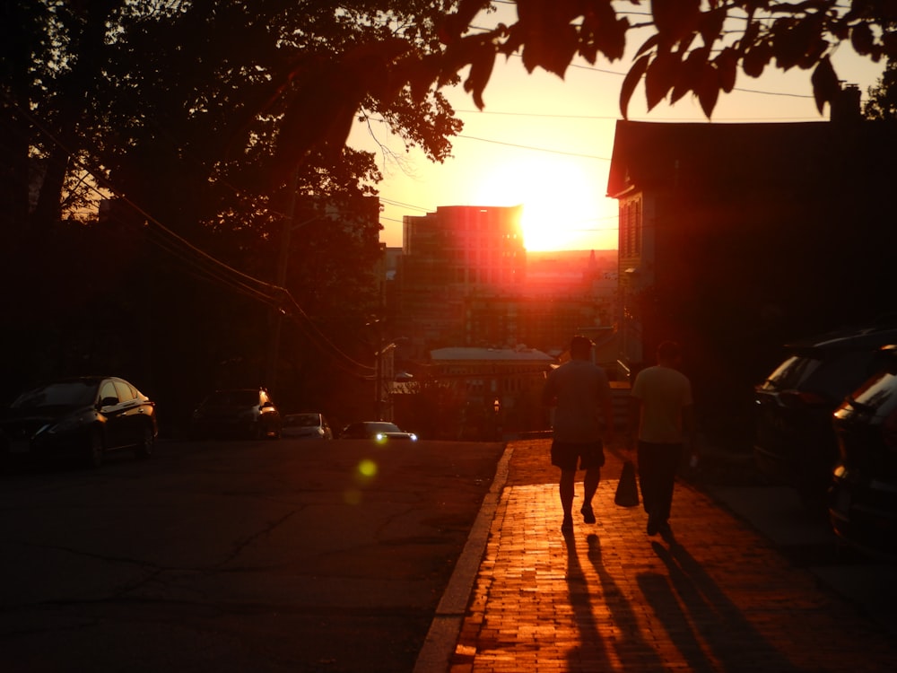 a couple of people walking down a street at sunset