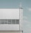 A modern industrial building facade featuring a vertical metal ladder on the right side and horizontal windows with closed blinds. The building exterior is made of light grey metal panels.