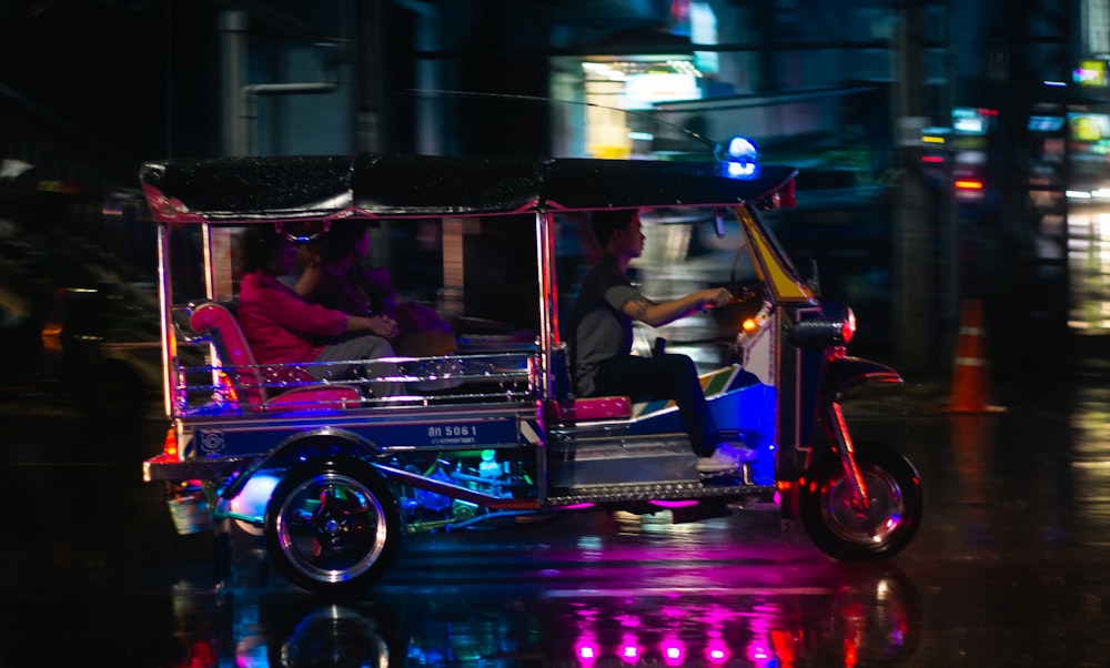 a three wheeled vehicle with two passengers on a city street at night