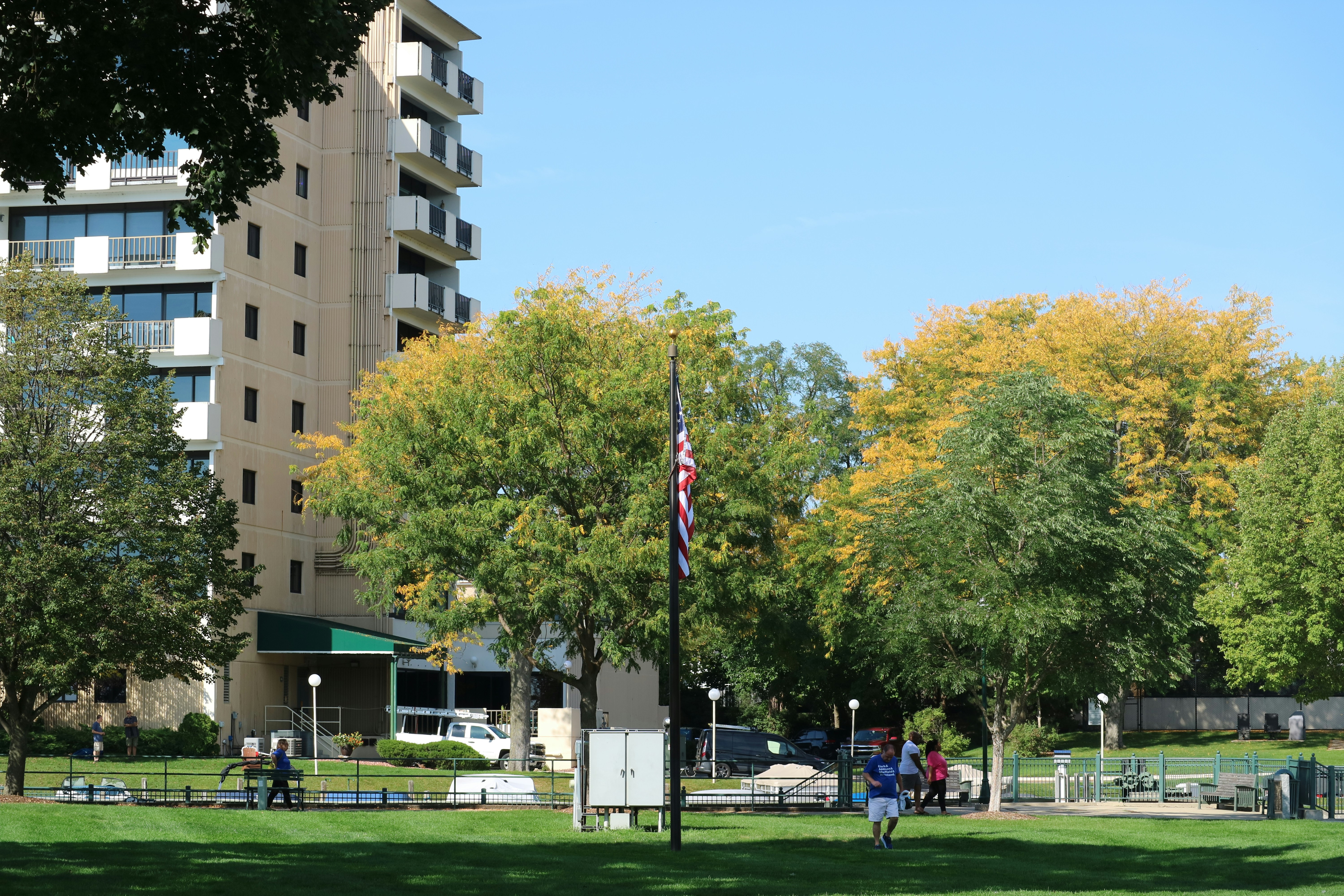 a group of people walking through a park next to a tall building