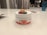 A white container labeled 'CBD + THC Gummies' with colorful gummy candies on top. The lid has three gummies in orange, red, and green. The setting is a modern kitchen with a blurred background featuring kitchen appliances and a blue glass.