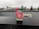 A package of ‘Hometown Hero’ stands prominently on a wet black surface, with a blurred cityscape featuring tall buildings and overcast skies in the background. The packaging design is vibrant with red and green colors, including images of watermelon slices. The text on the package highlights that it supports veterans and mentions ‘Delta 8’.