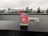 A package of ‘Hometown Hero’ stands prominently on a wet black surface, with a blurred cityscape featuring tall buildings and overcast skies in the background. The packaging design is vibrant with red and green colors, including images of watermelon slices. The text on the package highlights that it supports veterans and mentions ‘Delta 8’.